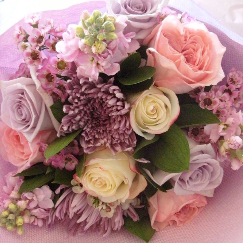 Mauve Mist.  Soft tones of purples, pinks and creams.  A wistful arrangement of roses, chrysanthemums and stocks with wax-flower and foliage fillers.  Wrapped in layered pink embossed paper with a fabric outer and complimenting ribbons.